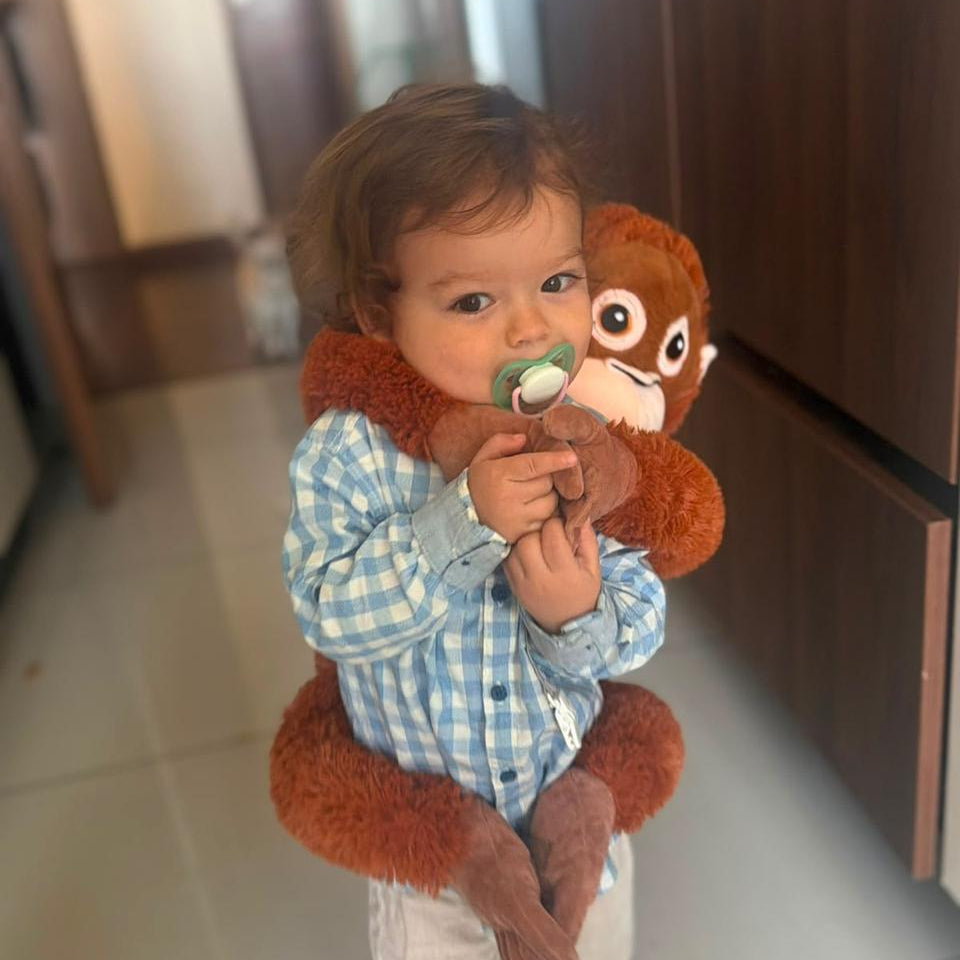Niño de pie abrazando el peluche mono XL, que le llega del pecho a los pies